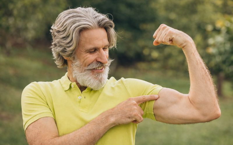 Idoso observando a musculatura do braço como exemplo de preservação da massa muscular na terceira idade